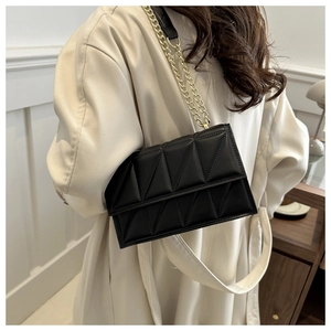 Detail shot of black quilted shoulder bag with golden chain strap on model in beige coat