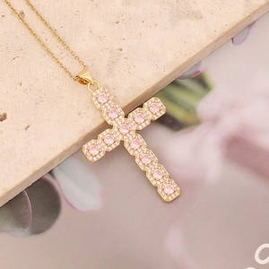 Detailed shot of golden cross necklace with pink zircon crystals on a stone plate