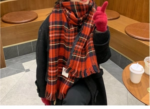 Detail of red plaid wool scarf with fringes worn by a model in a cozy cafe setting