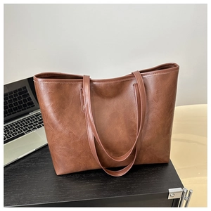 Detailed view of large dark brown retro tote bag placed next to a laptop on a desk