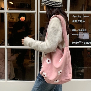 Detail of pink plush tote bag with white daisy patterns worn on shoulder in street setting