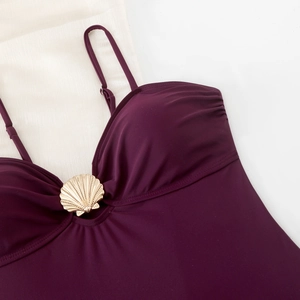 Detail of plum swimsuit featuring a metallic gold shell buckle and pleated fabric texture