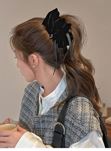 Detail view of large black velvet bow hair clip styled on a model's elegant ponytail