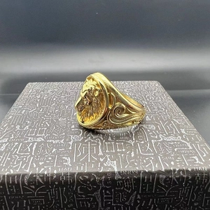 Detailed view of a gold-plated lion head ring on a textured grey jewelry box