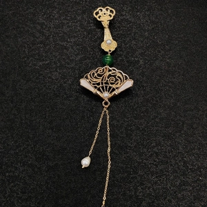Détail d'une broche chinoise en forme d'éventail doré avec perles et glands élégants