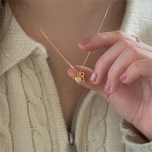 Close-up of a gold heart and key pendant necklace worn over a beige knit sweater