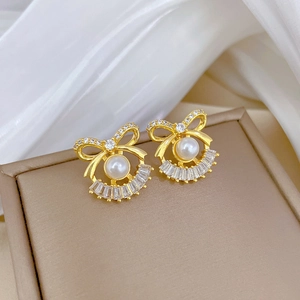 Detailed close-up of gold bow earrings with white pearl and sparkling rhinestones