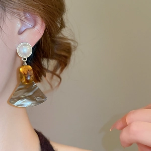 Close-up of three-tier drop earrings with pearls and amber resin fan-shaped pendants