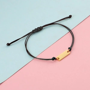 Close-up of adjustable black braided rope bracelet with a polished gold rectangle metal plate