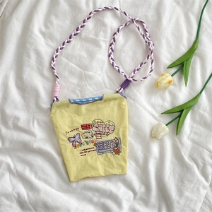 Gros plan d'un mini sac en toile jaune avec broderies et bandoulière tressée