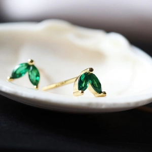 Macro detail of leaf-shaped gold stud earrings with green zircon gems on shell base