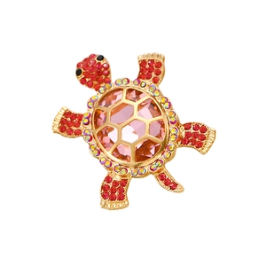 Détail de broche tortue dorée avec cristal rose et accents de strass rouges