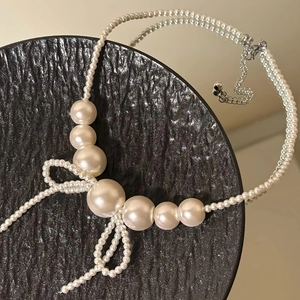 Elegant bow fringe pearl necklace with silver lobster clasp on black stone display