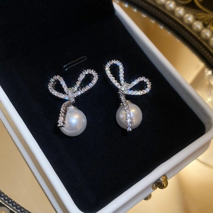 Detailed view of silver bow stud earrings with shimmering zircons and round pearls