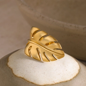 Detailed view of a gold monstera leaf ring on a ceramic pottery edge in warm light