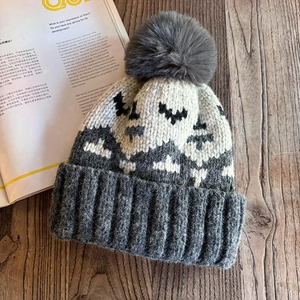 Macro detail of wave patterned knit beanie with a soft faux fur pompom on wooden surface