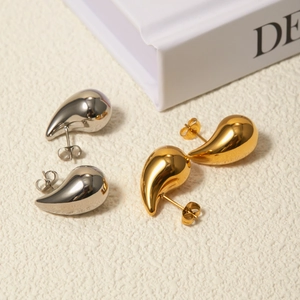 Polished 18k gold and silver teardrop earrings on a minimalist cream fabric background