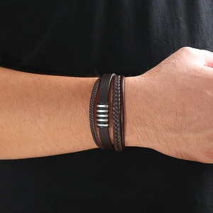 Close-up of a layered dark brown braided leather bracelet with silver metal ring charms