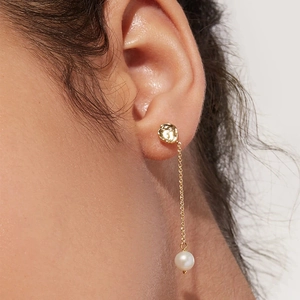 Close-up of elegant gold tassel chain earring with a round white pearl on model