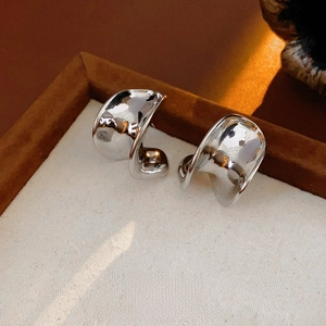 Minimalist silver C-shape wavy metal stud earrings displayed on a luxury velvet tray