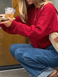 Detail of red crewneck knitted sweater and straight blue jeans in a casual street style