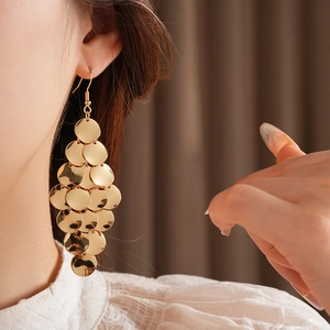Close-up of golden round sequin tassel earrings worn by a model in a soft lighting