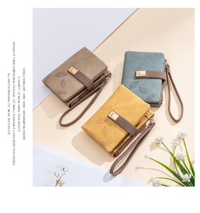 Close-up of matte faux leather wallets with leaf embossing and metal charms in multiple colors
