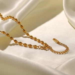 Close-up of golden oval bead chain necklace with extension on soft silk background