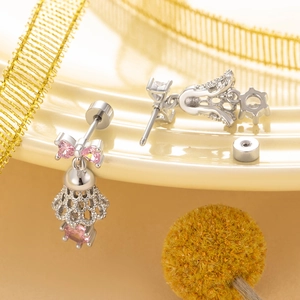 Silver bow bell earrings with pink heart zircon stones on a beige ceramic plate