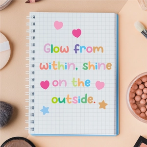 Aesthetic grid notebook with colorful glow within quote and cosmetic props on peach surface