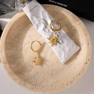 Close-up of golden sun charm hoop earrings with crystal accents on a stone tray