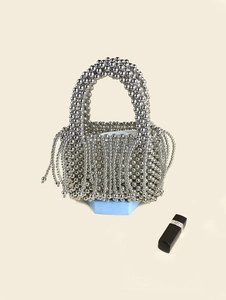 Silver beaded bucket bag with fringe details and woven metallic pearls on blue pedestal