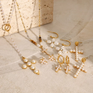 Gold stainless steel jewelry set with pearl cross necklaces and earrings on stone background