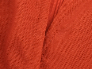 Detailed macro view showing the orange-red woven fabric texture and stitching of the dress