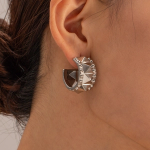 Macro shot of silver C-shaped stud earrings with 3D pyramid rivet texture on a model
