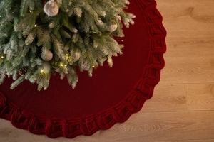 Detail of red cable-knit Christmas tree skirt on wooden floor showing soft woven texture