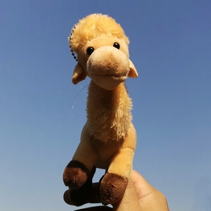 Close-up of a cute yellow plush camel keychain against a clear blue sky background.