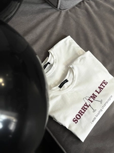 T-shirt bianca minimalista con stampa slogan champagne su sfondo grigio strutturato