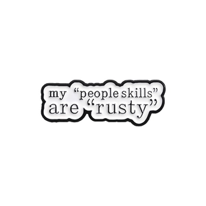 Detail of white enamel pin featuring humorous black text My people skills are rusty