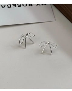 Macro detail of silver bow stud earrings with minimalist metal finish on paper card