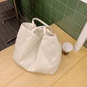 Detail of a creamy white large tote bag with herringbone texture and thick rope handles
