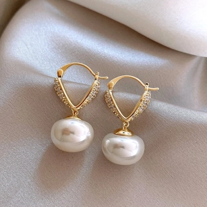 Detailed close-up of gold-plated V-shaped earrings with crystals and large white pearls