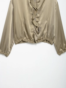 Detailed close-up of golden satin jacket with elastic hem and front zipper closure