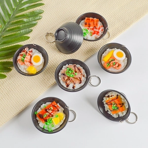 Handcrafted miniature Japanese eel and seafood rice bowl keychains on a rustic fabric background
