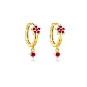 Detailed close-up of golden floral hoop earrings with sparkling red gemstone drops