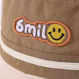 Detailed close-up of khaki kids bucket hat with embroidered smiley patch and Smil text