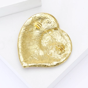 Détail du dos d'une broche cœur dorée montrant la texture radiale et le fermoir à épingle