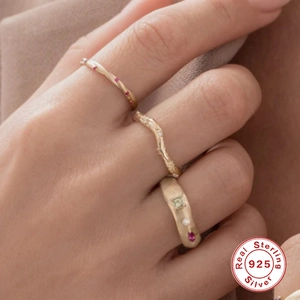 Three stackable gold S925 silver rings with red, white, and green gemstones on model hand