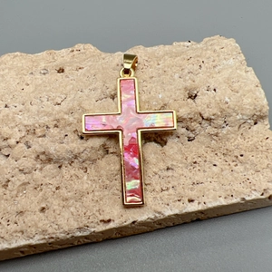 Elegant gold cross pendant with iridescent pink shell inlay on a natural stone base
