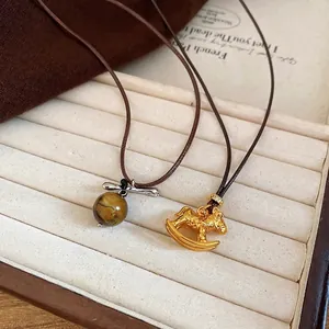 Vintage tiger eye bead and golden pony pendant necklace with leather cord on fabric background